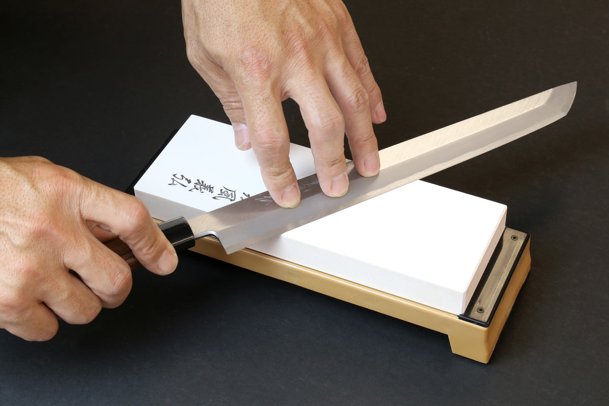 Sharpening whetstone on beige base, white stone block guided by hands