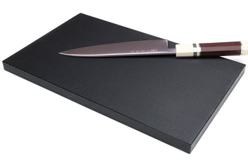 Black rectangular cutting board with chef knife lying across surface