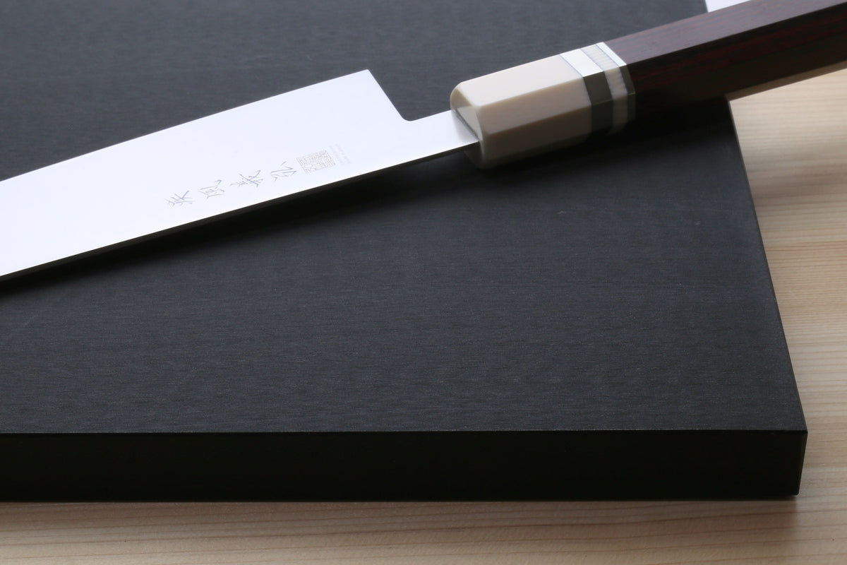 Japanese chef's knife on a black cutting board, close-up on a wooden counter