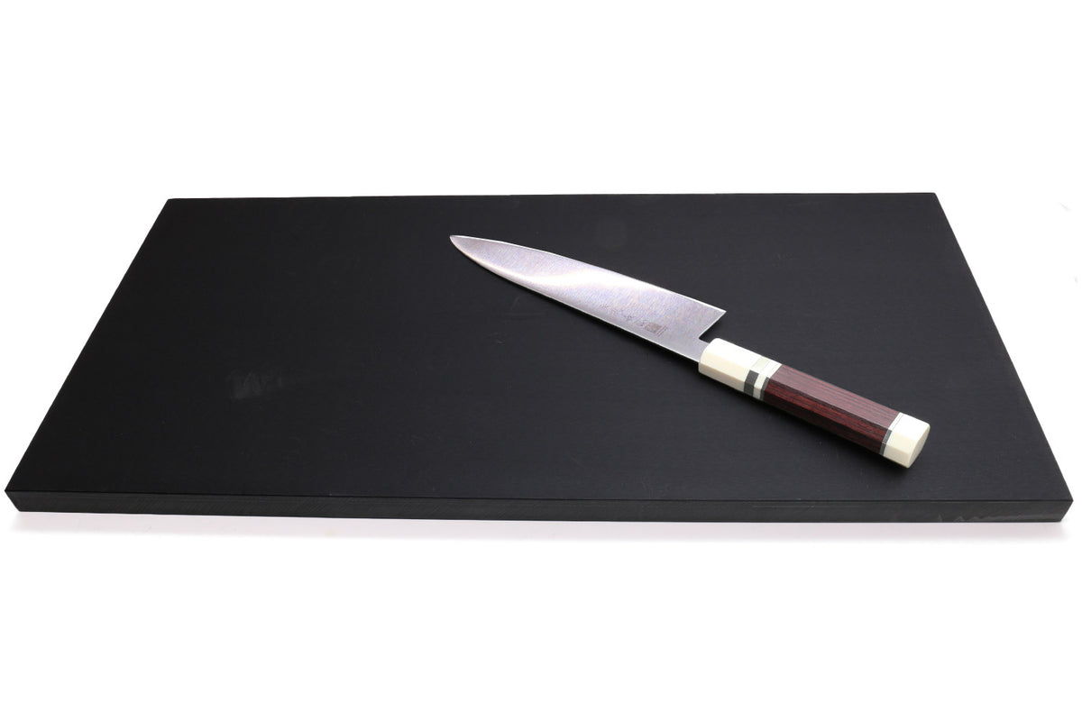 Black rectangular cutting board with chef knife resting on top