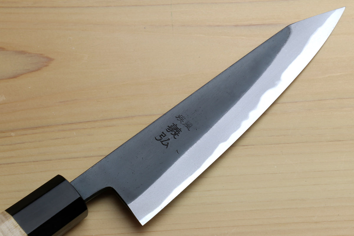 Kurouchi-finished blue steel knife blade with visible engraved mark and light edge.