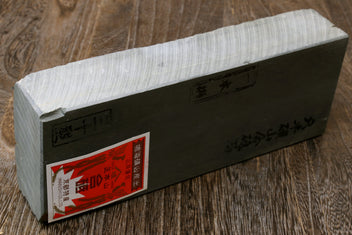 Light gray sharpening whetstone block with red-orange label and engraved markings