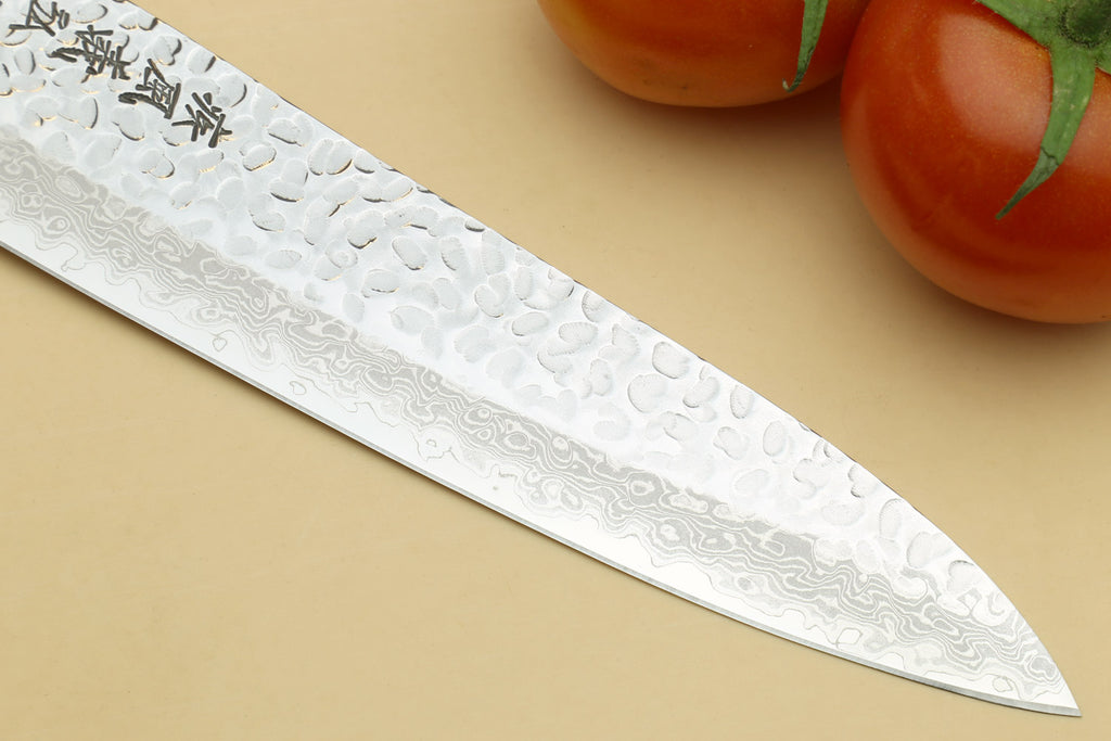 Decorative knife blade with engraved patterns on a beige background with tomatoes.
