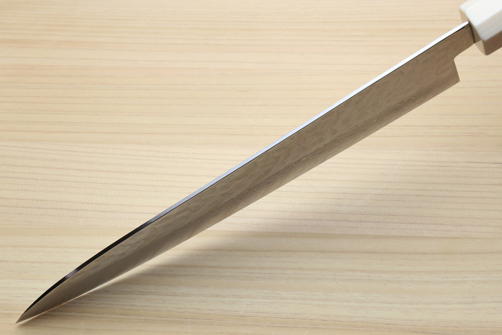 A close-up of a Japanese-style kitchen knife with a satin-finished steel blade and a white handle, resting diagonally on a light wood grain surface.