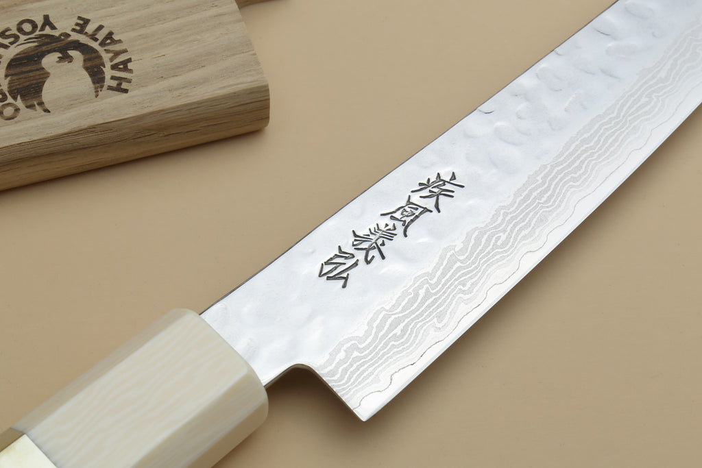 Damascus petty knife showing blade etching and ivory handle with beige cutting board
