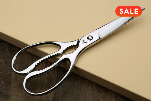 Stainless scissors on a beige cutting board and a red 'SALE' label.