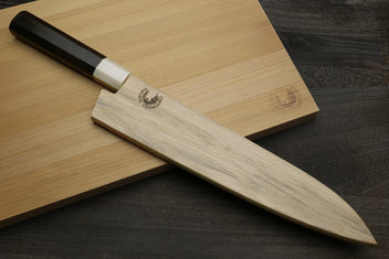 Gyuto chef's knife resting on wooden boards, dark handle and black-patterned blade