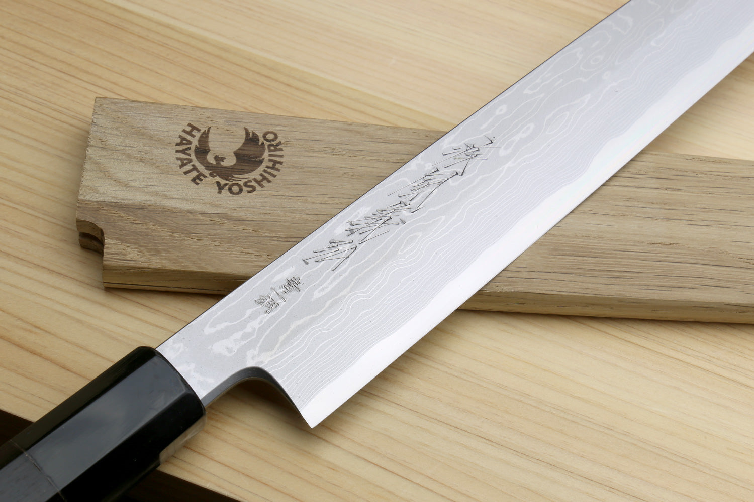 Damascus yanagi knife with a sheath and blade featuring engraved text on a cypress cutting board
