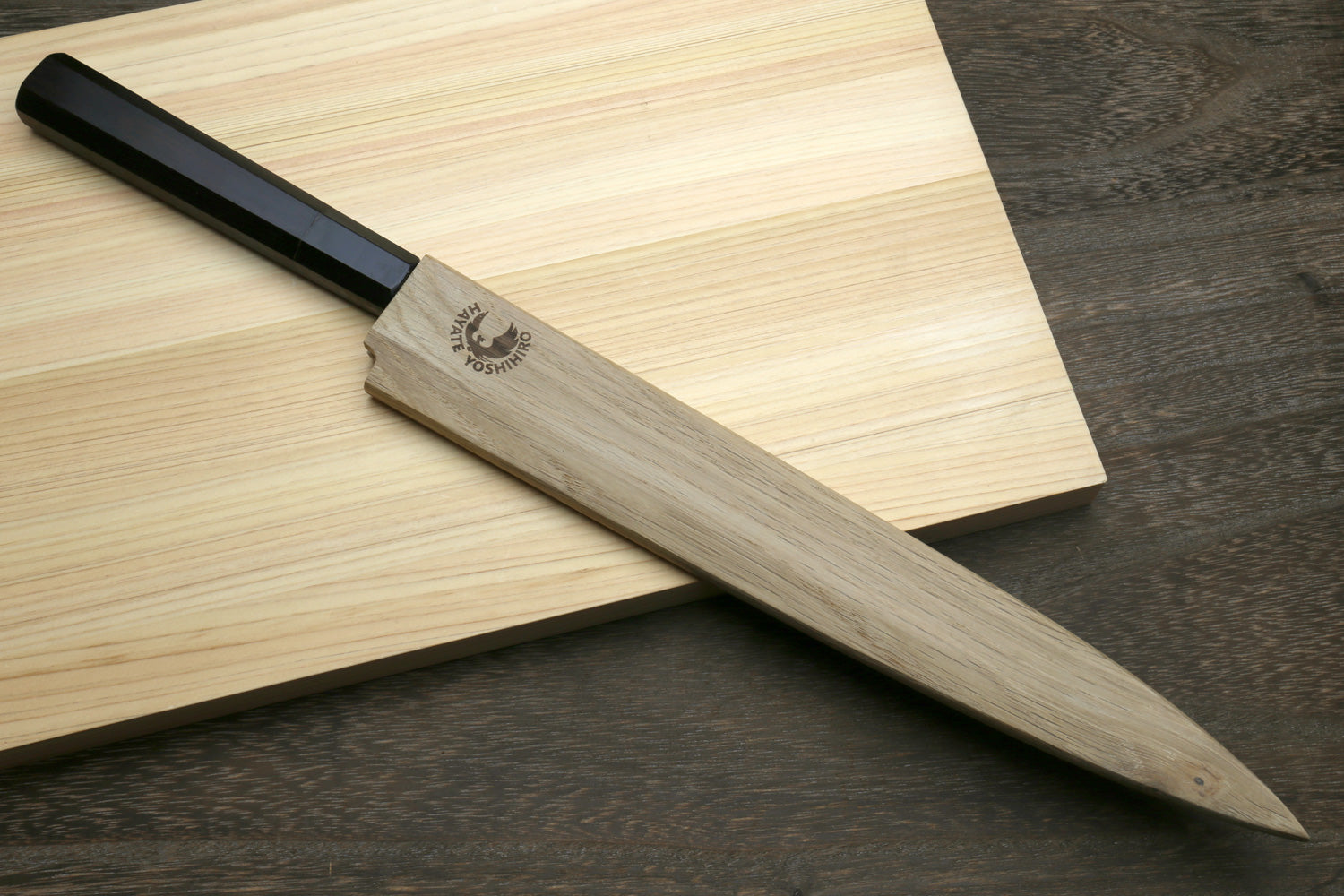 Yanagi knife with an ebony handle stored in a wooden sheath on a wooden cutting board.
