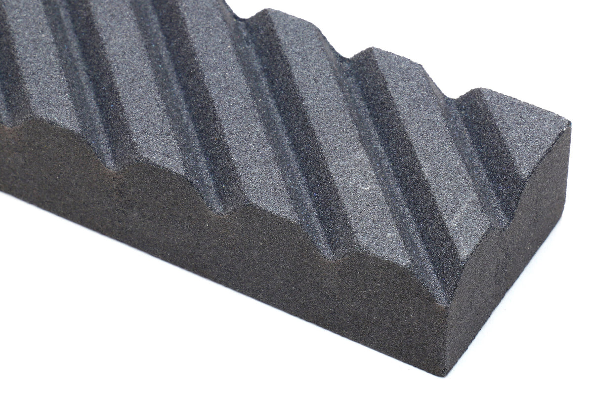 Close-up of a black sharpening stone edge with parallel grooves and ridges