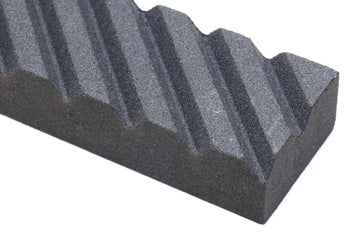 Close-up of a black sharpening stone edge with parallel grooves and ridges