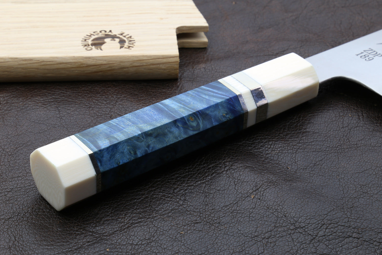 Knife handle with a blue and white, a knife sheath on a side of the handle on a dark surface 