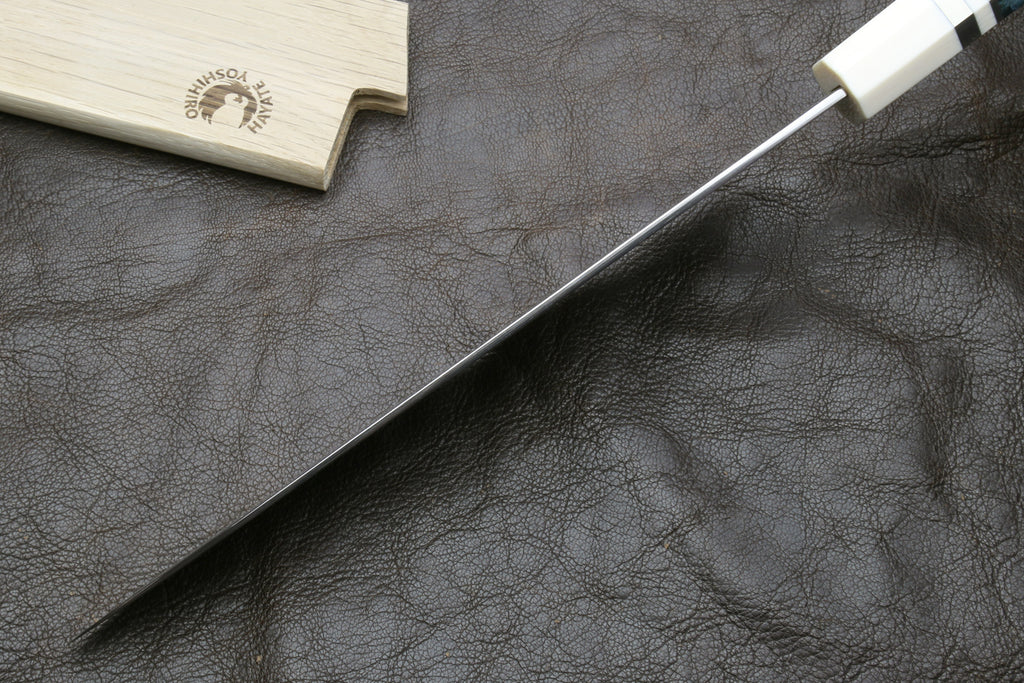 Spine of a knife blade on a dark surface, accompanied by a wooden sheath
