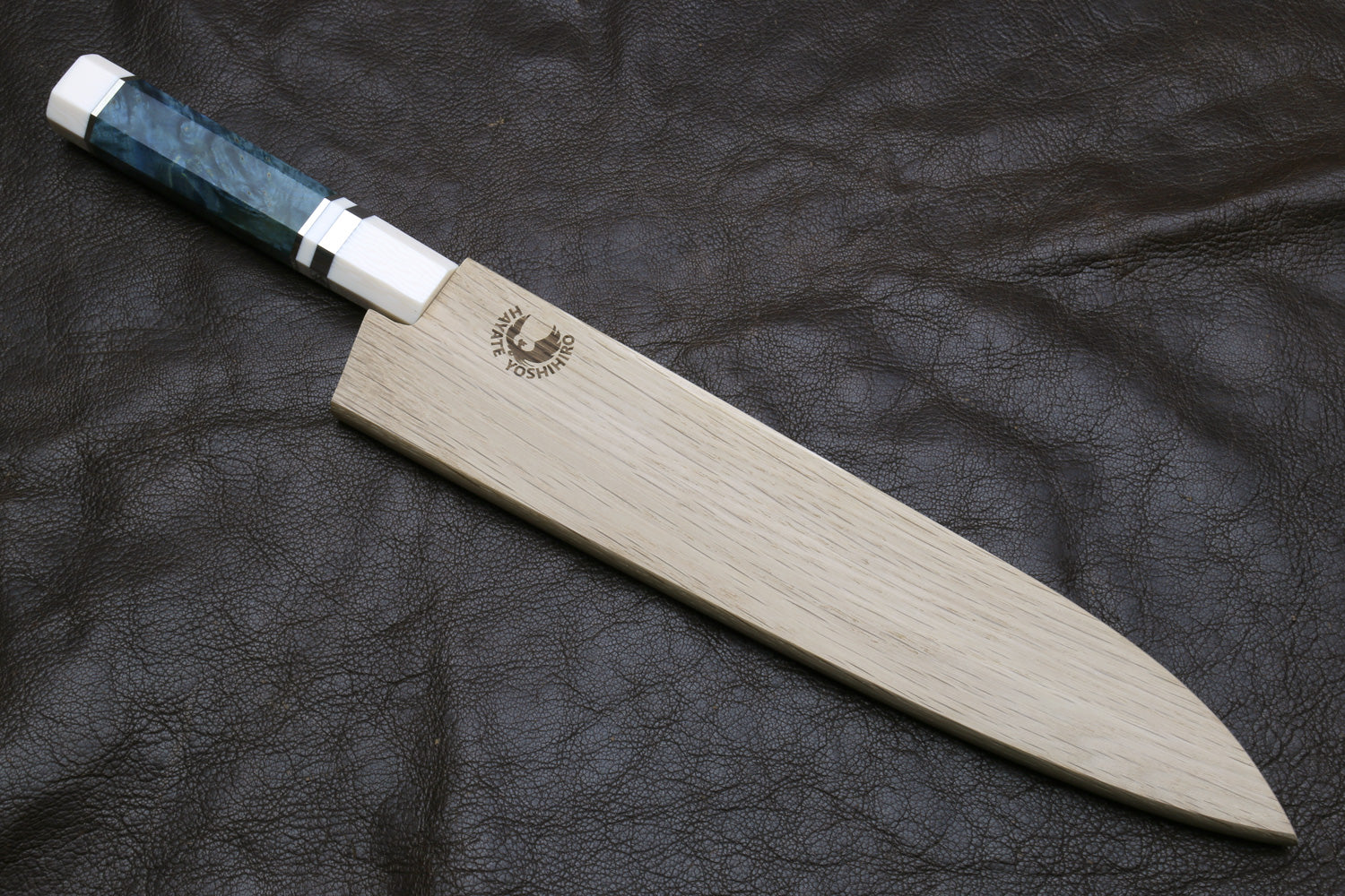 knife with a wooden blade and white handle stored in a wooden sheath on a dark textured background