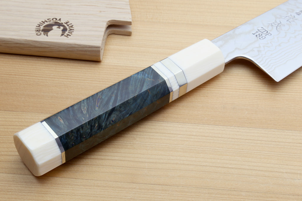 a beautiful handle of ZDP189 damascus knife, accompanied by a wooden sheath on a light wooden surface