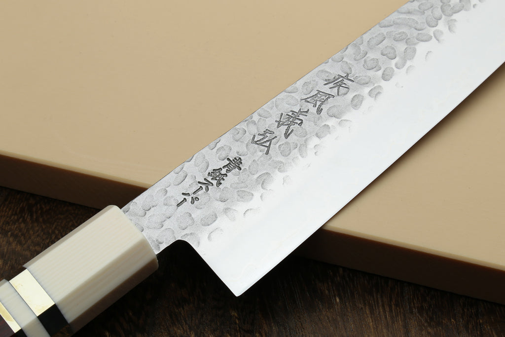 Chef's gyuto knife blade close-up with hammered finish and etched markings; ivory bolster