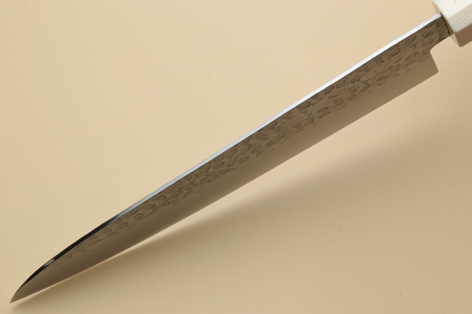 Chef's gyuto knife tip close-up with hammered stainless steel blade and ivory bolster