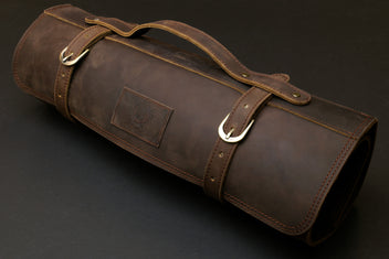 Brown leather knife roll case with top carry handle, side label patch, and metal rings.