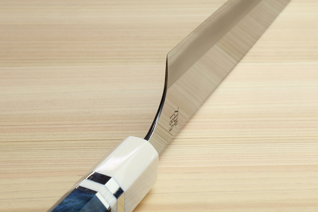 A close-up of a Japanese-style kitchen knife with a satin-finished steel blade and a white handle featuring a dark blue inlay, resting diagonally on a light wood grain surface.