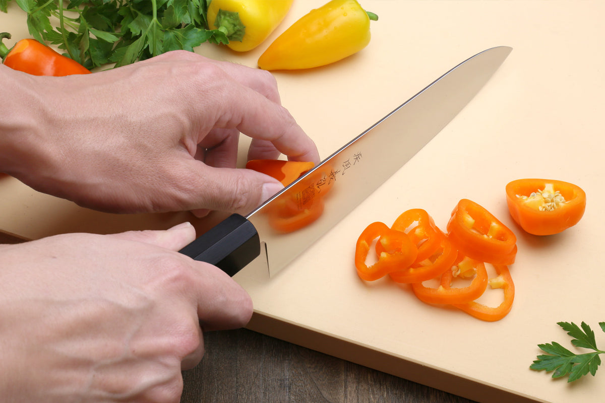Chef knife slicing bell pepper on a cutting board, rosewood handle and ivory bolster