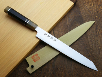 Sujihiki kiritsuke knife with white blade, dark horn handle, and wooden sheath on boards.
