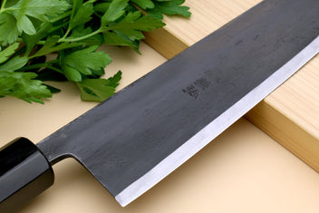Gyuto chef knife close-up: dark blade with cutting edge and mark near heel
