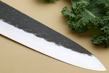 Gyuto chef's knife blade close-up, black-speckled finish and white cutting edge