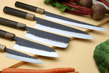 Stainless clad knife set with five blades and dark composite handles on a wooden board