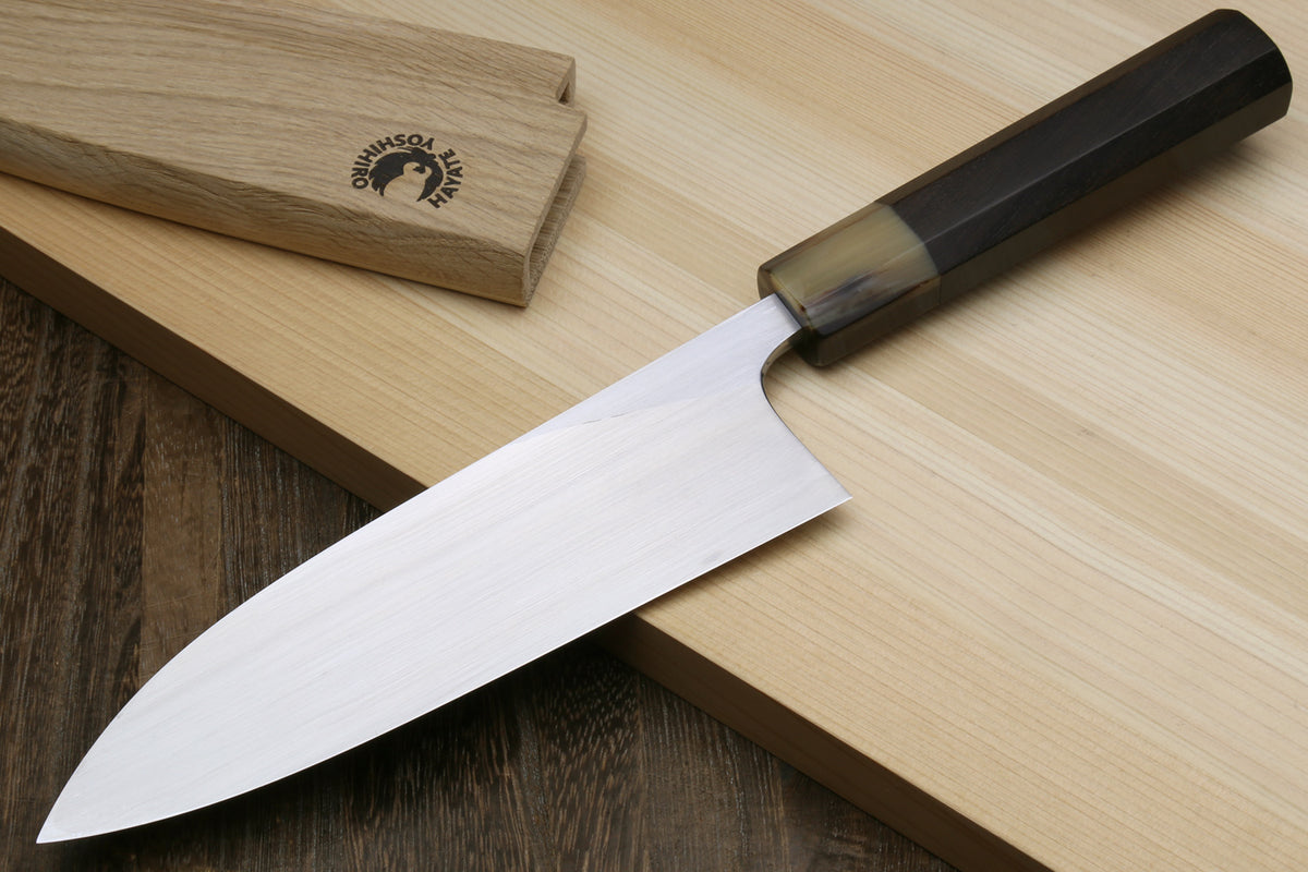 Deba fish fillet knife with white blade and dark handle, angled on light wood