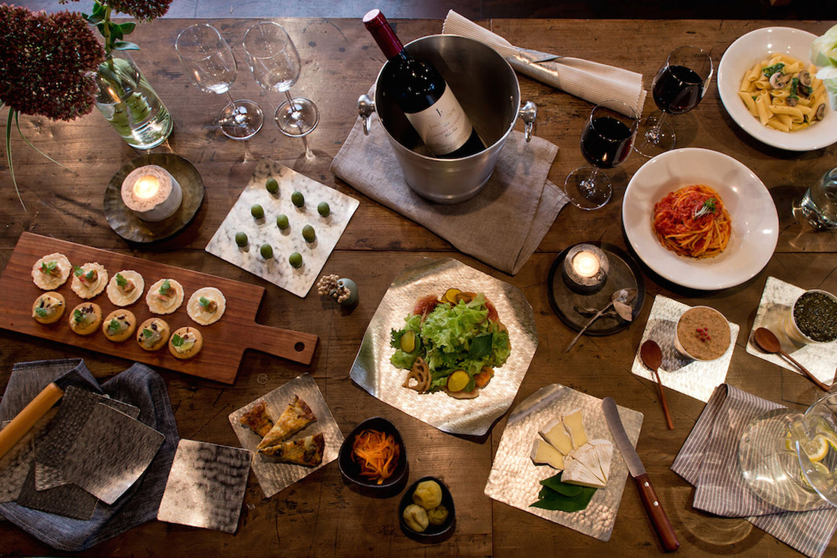 Multiple flexible tin plates with small dishes, drinks, and serving utensils