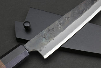 Kurouchi-finished steel petty blade with engraved characters and dark handle end.