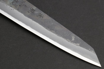 Petty utility knife tip with kurouchi-finished steel and small engraved mark.
