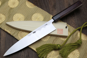 Japanese chef knife with light saya, dark handle, and green tassel cord