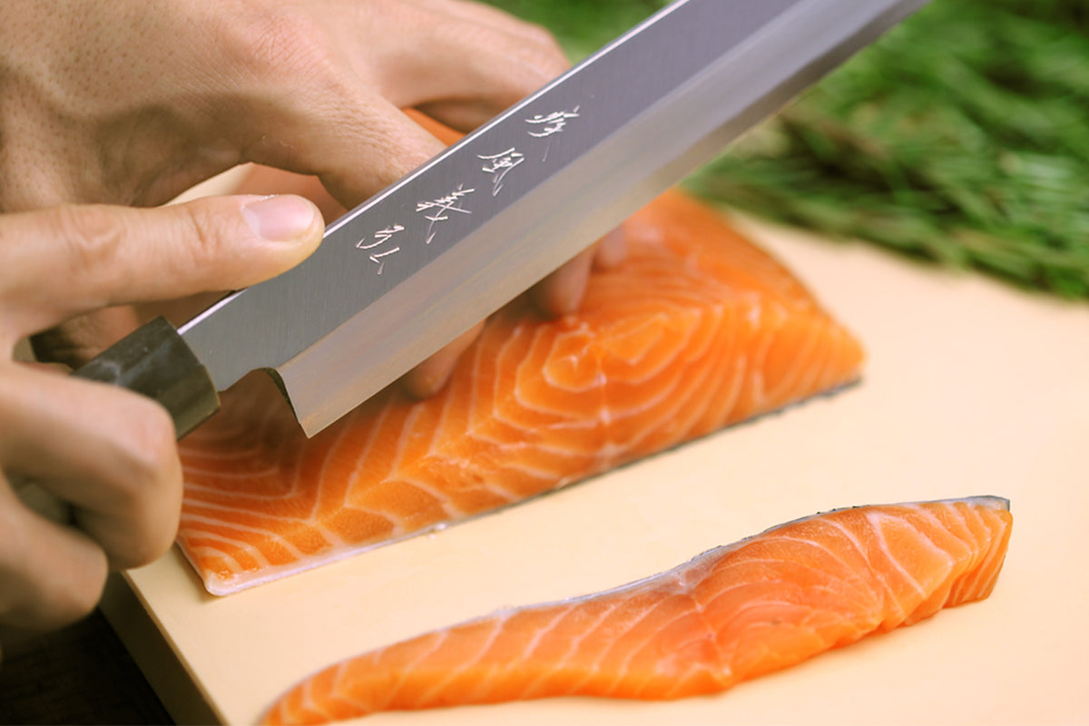Beige cutting board with salmon fillets being sliced with a chef’s knife