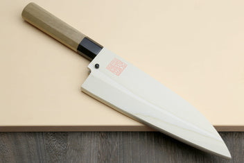 Deba chef knife on board with white blade, light wood handle, and black bolster