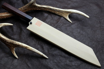 Japanese chef knife with pale blade and dark handle, angled on dark leather