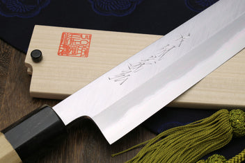 Japanese chef knife with white steel blade close-up and magnolia handle, green tassel cord.
