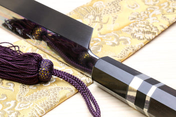 Japanese yanagiba sushi knife close-up: mirror-finished blade, black handle, silver striped bands