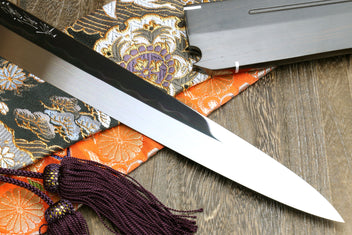 Sashimi knife with mirror-finished blade and saya, purple cord tassel on patterned fabric