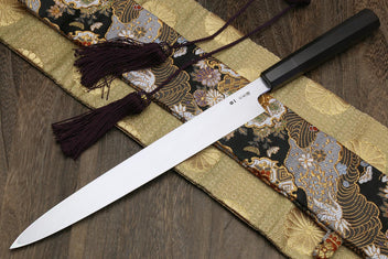 Yanagi knife with white steel blade and dark handle on gold and black patterned cloth