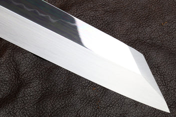 Mirror-polished knife blade close-up with sharp tip.