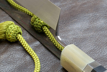 Knife handle close-up with ivory wrap and silver-toned bands, green cord.