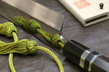 Japanese-style kitchen knife with wavy steel blade beside light wood sheath