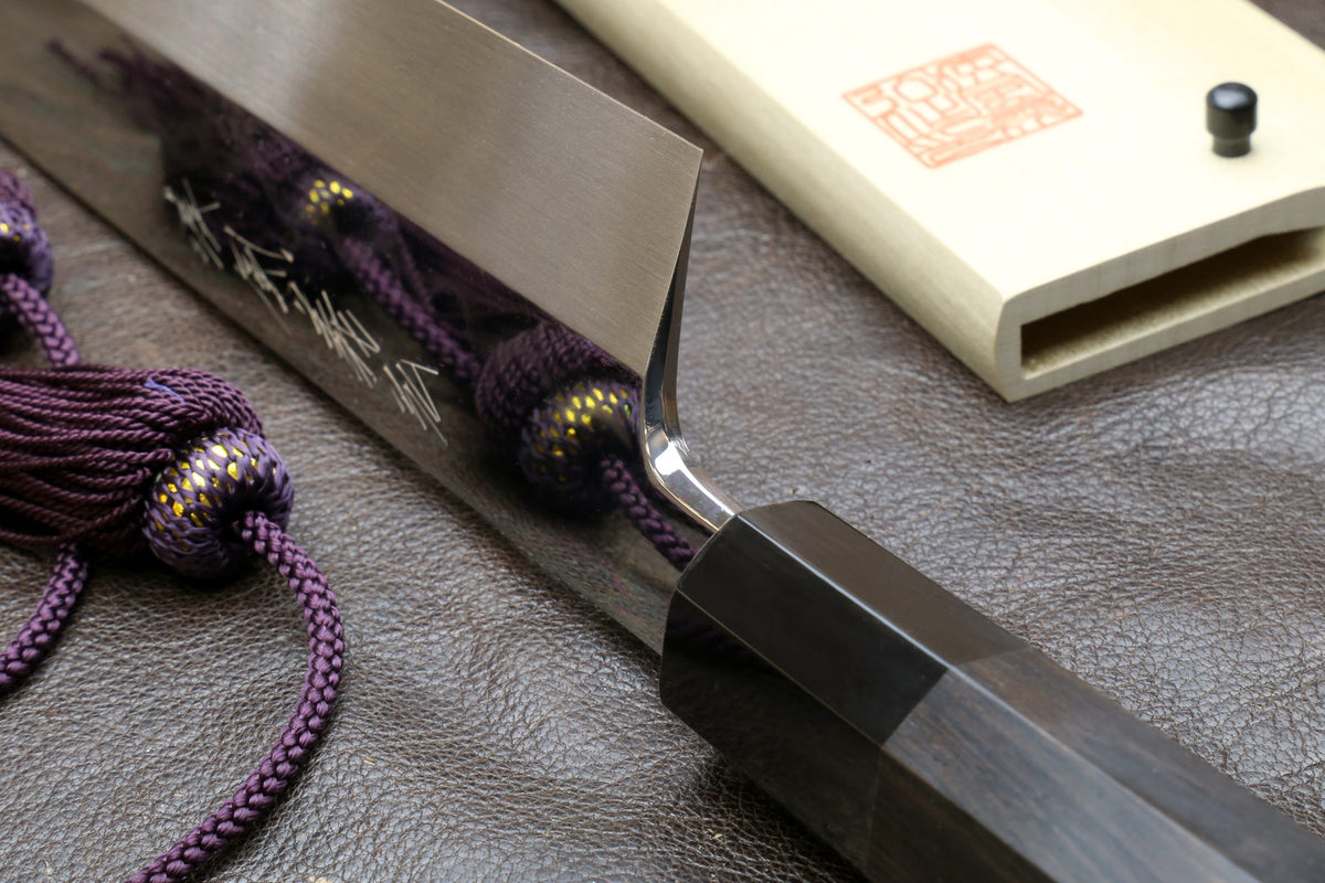 Kiritsuke knife and saya with dark handle; mirror-polished blade near the sheath
