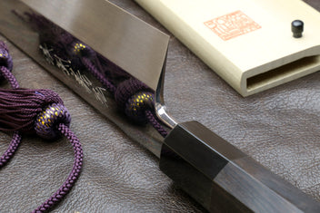 Kiritsuke knife and saya with dark handle; mirror-polished blade near the sheath
