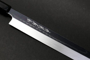 Japanese knife blade close-up with mirror-finished steel and etched pattern near the spine.