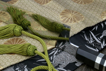 Gyuto chef knife close-up with mirror blade and ebony handle, shown with green cords