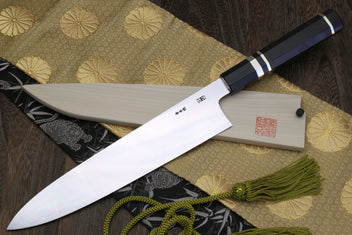 Gyuto chef knife with mirror-polished blade and ebony handle, lying on patterned cloth