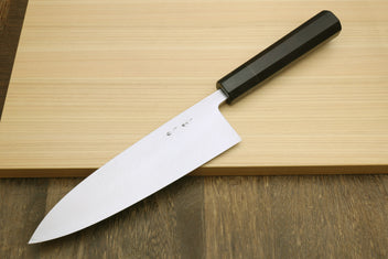Japanese chef knife with curved silver blade and black handle, on light wooden board