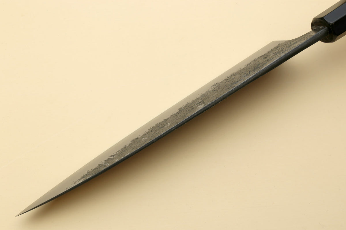 Gyuto knife side view with white steel blade and dark bolster, pointed tip.